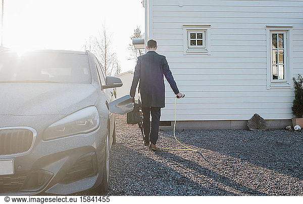 man walking with electric car lead leaving for work in the morning