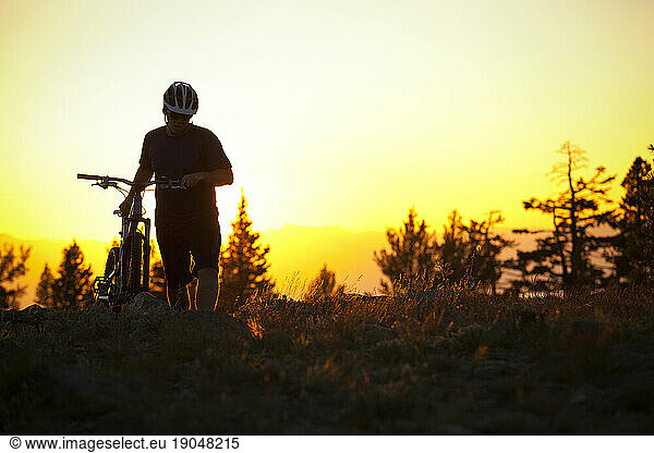 Man walks mountain bike at sunset
