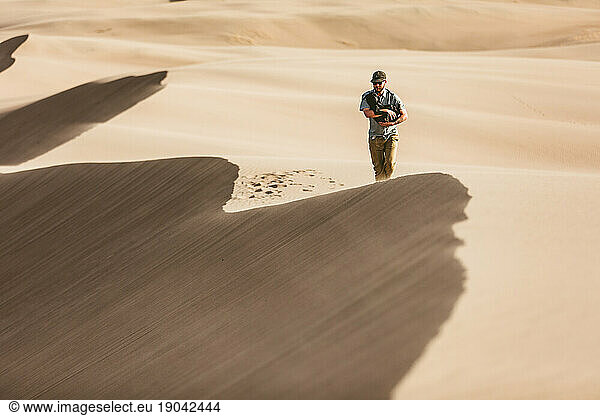 man walks with his puppy along windy sandy ridge line of sand dunes