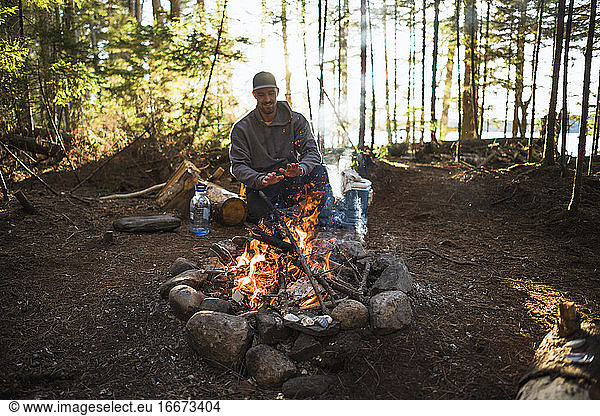 Man warming by the fire at sunset while car camping in coastal Maine