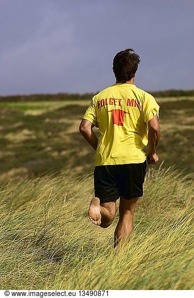 Man wearing a yellow T-shirt  Folget Mir  Follow me  while running over a dune  Brittany  France  Europe