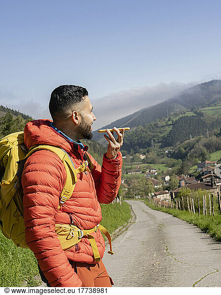 Man wearing backpack sending voicemail through mobile phone on sunny day
