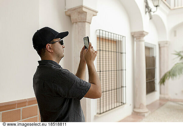 Man wearing cap photographing through smart phone