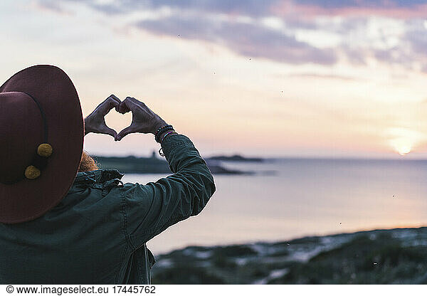 Man wearing hat gesturing heart shape at beach
