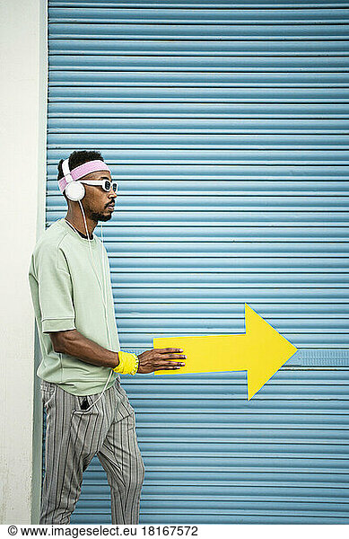 Man wearing headphones listening to music walking with yellow arrow sign by blue shutter