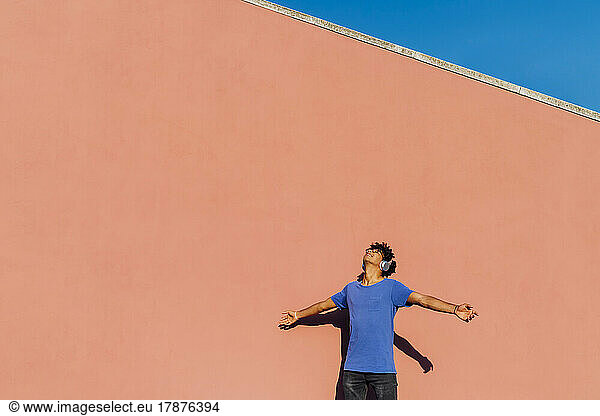 Man wearing headphones standing with arms outstretched on sunny day