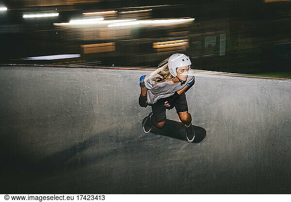 Man wearing helmet while skateboarding on sports ramp at night