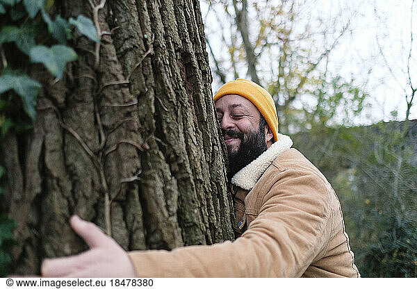 Man wearing knit hat hugging tree in forest