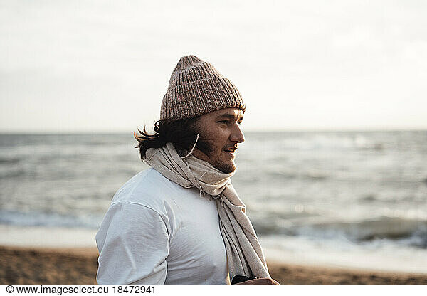 Man wearing knit hat standing in front of sea at beach