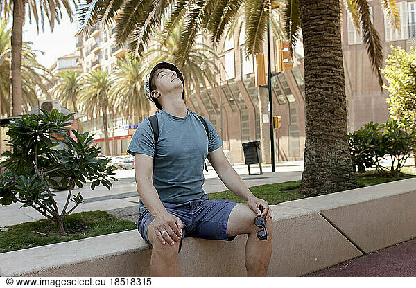 Man wearing panama hat sitting with eyes closed near palm trees
