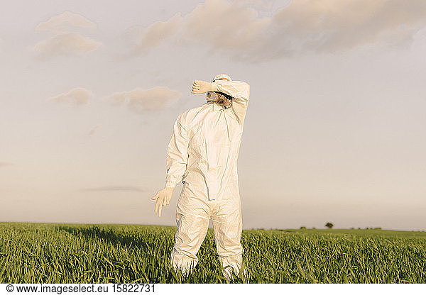 Man wearing protective suit and mask in the countryside covering his eyes