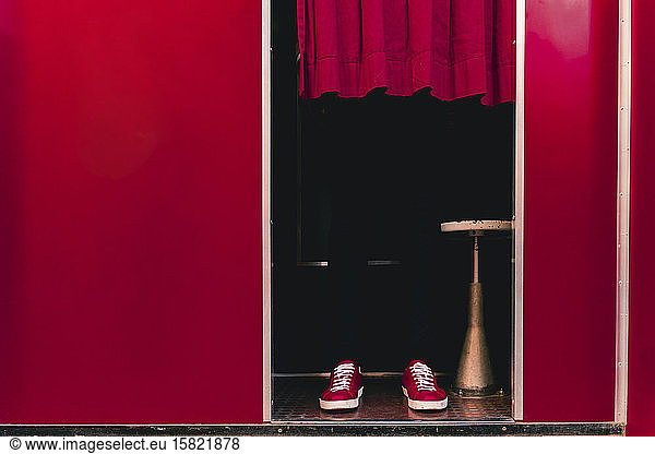 Man wearing red sneakers standing behind curtain in a photo booth