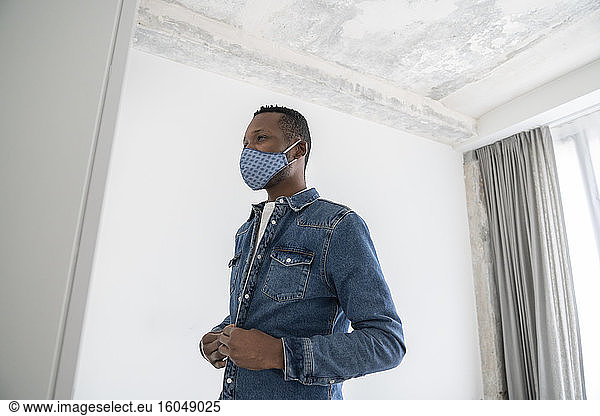 Man wearing reusable face mask indoors putting on his jeans jacket