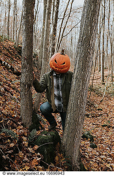 Man wearing scary carved pumpkin head in the woods for Halloween.
