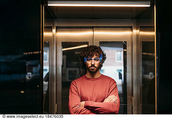Man wearing smart glasses standing with arms crossed in front of elevator