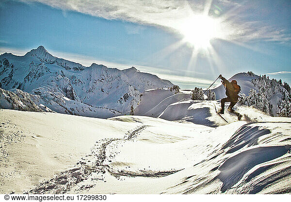 Man wearing snowshoes jumps off a mountain ridge.