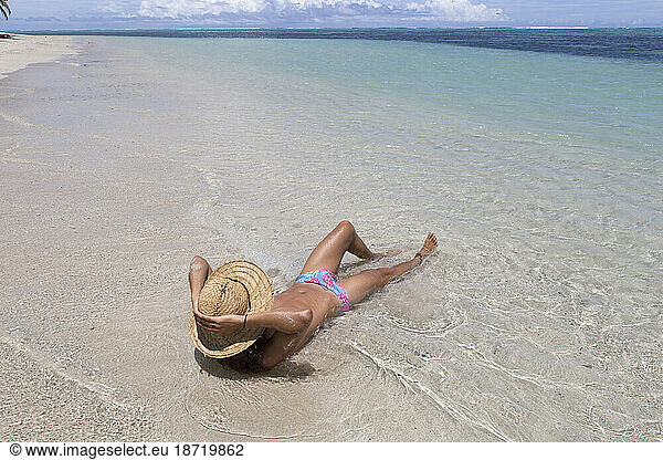 Man wearing straw hat and blue speedo  tanning on idyllic sandy beach