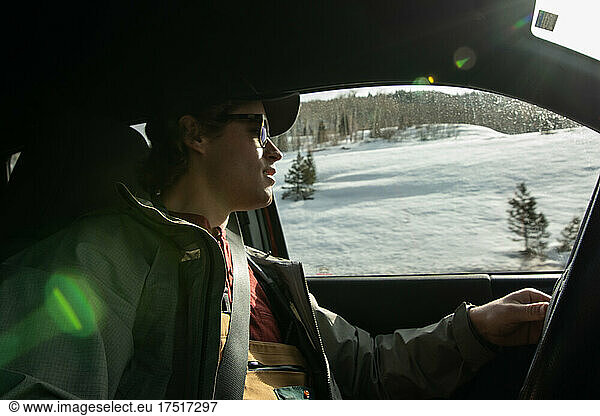 Man wearing sunglasses driving through snowy mountains