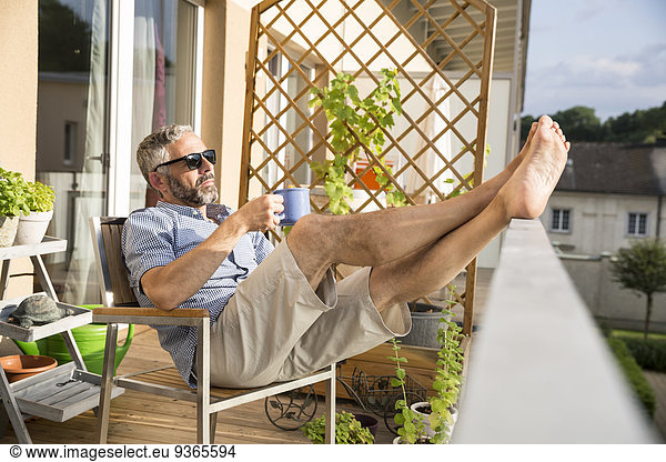 Man wearing sunglasses relaxing on his balcony with a cup of coffee