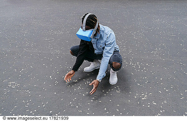Man wearing virtual reality headset crouching on road