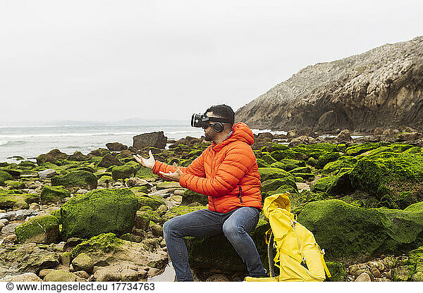 Man wearing virtual reality simulator gesturing sitting on rock