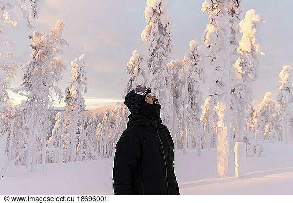 Man wearing warm clothing looking up standing in snow