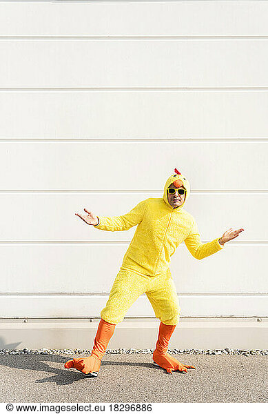 Man wearing yellow chicken costume gesturing in front of wall