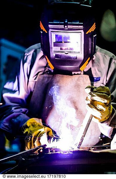 Man welding in a workshop with yellow gloves and black mask