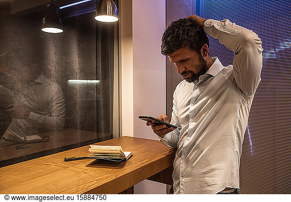 Man with a beard and moustache looking at a mobile phone with his hand on his head.