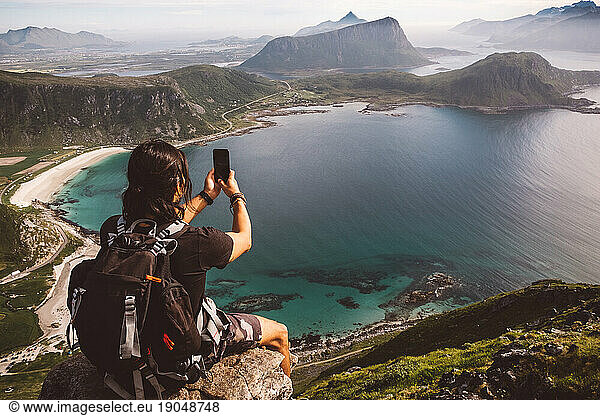 Man with a cellphone sitting in a rock taking photos of the view