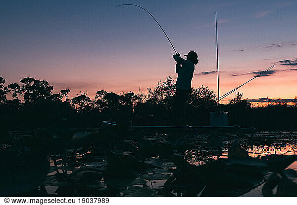 Man with a fish on the line at Sunset