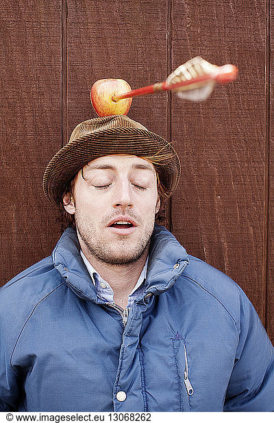 Man with apple on head against wooden wall