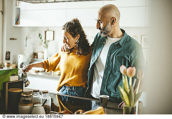 Man with arm around woman standing in kitchen at home