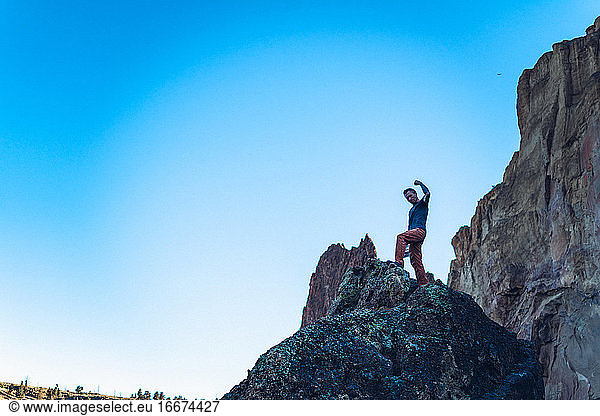 Man with arm up on the top of the boulder in Smith Rock park in Oregon