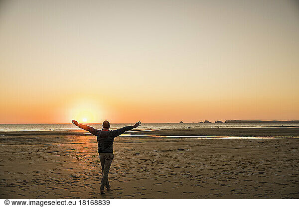 Man with arms outstretched enjoying on shore at sunset