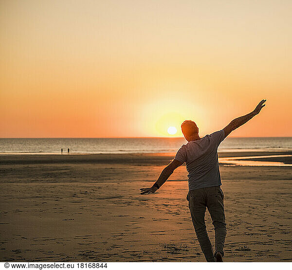 Man with arms outstretched having fun on beach at sunset