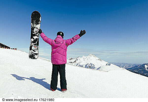Man with arms raised holding snowboard in winter on sunny day