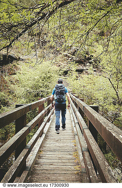 Man with backpack and cap crossing a bridge