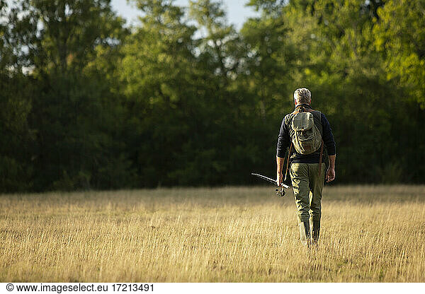 Man with backpack and fly fishing pole walking in rural field
