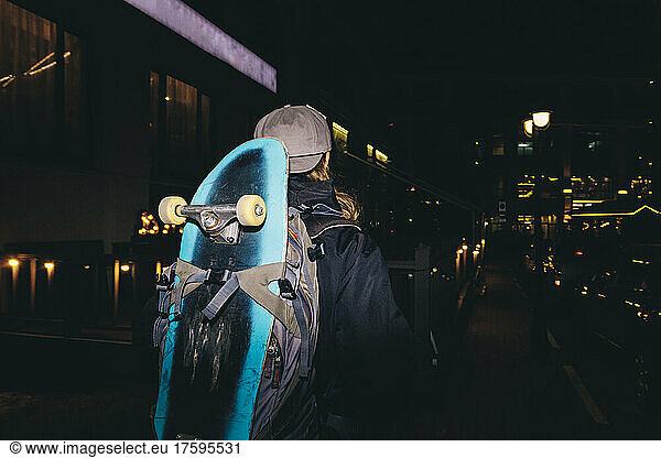 Man with backpack carrying skateboard at night