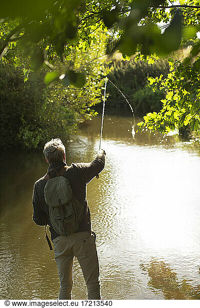 Man with backpack casting fly fishing pole at river
