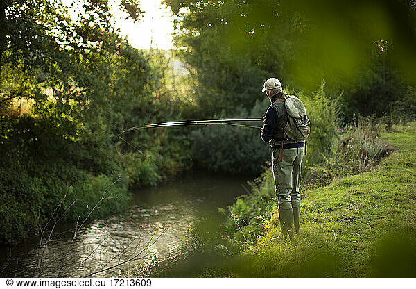 Man with backpack fly fishing at riverbank