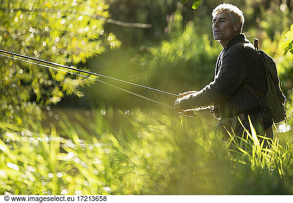 Man with backpack fly fishing with pole among sunny grass