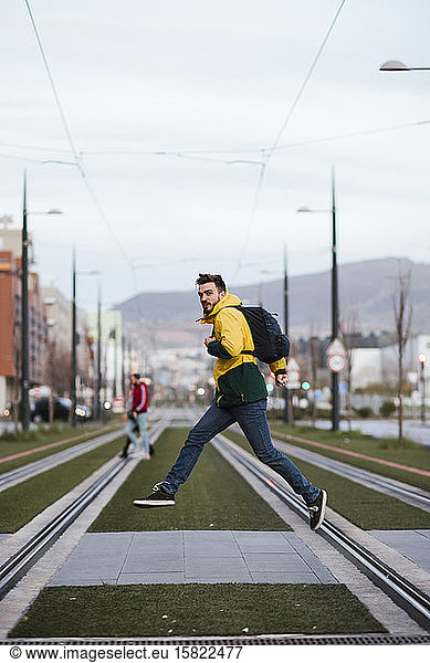Man with backpack in the city jumping on tram tracks