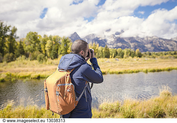 Man with backpack photographing while standing at riverbank