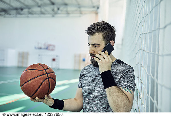 Man with basketball using smartphone  indoor