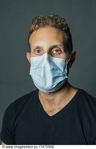 Man with blond hair wearing protective face mask against gray background