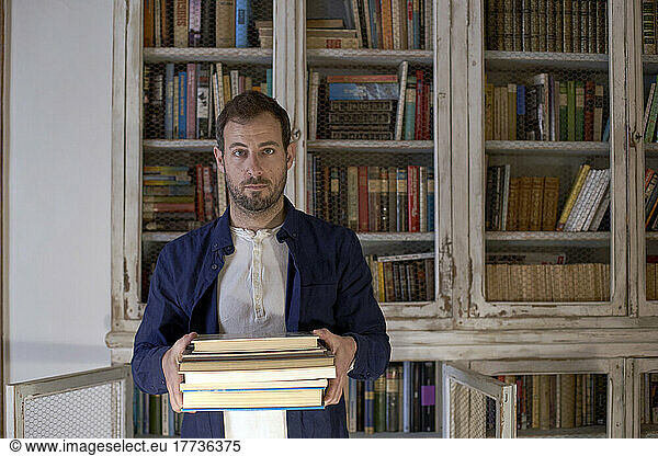 Man with book in front of bookshelf