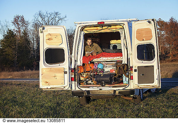 Man with book looking away while relaxing in camper van