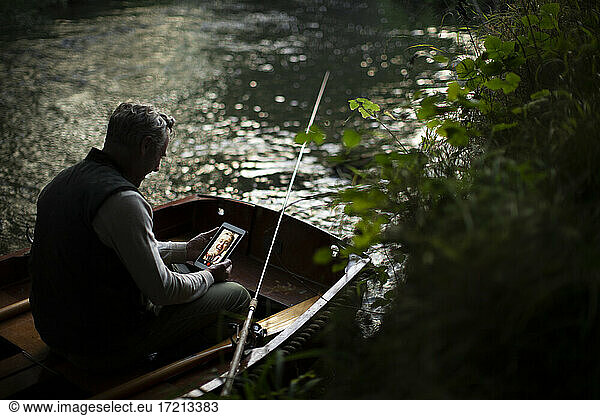 Man with digital tablet fly fishing and video chatting in boat on river
